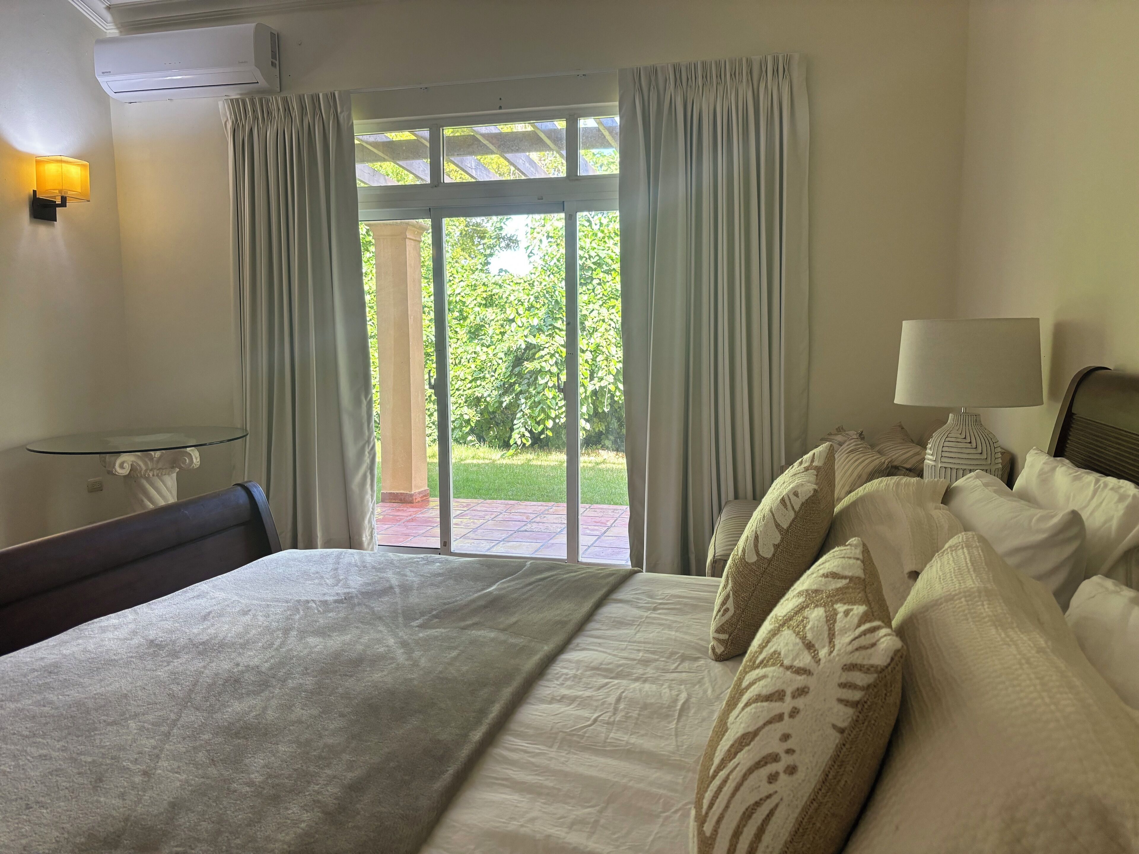 Camera d'albergo con un letto, una lampada, un tavolo e vista su un giardino dalla finestra.