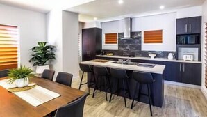 A modern kitchen with dark cabinets, a central island, and a dining area with a wooden table and chairs.