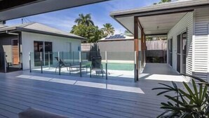 A modern outdoor deck with a pool, glass balustrades, and a covered patio area.