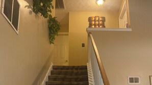 A carpeted staircase with a wooden handrail, a white door at the top, and a wall-mounted plant. - Enchanting Cottage Home nearby Airport (Conley)