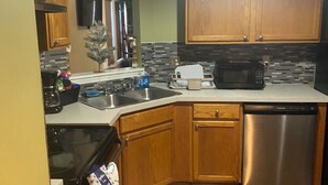 A kitchen with wooden cabinets, a stainless steel dishwasher, a microwave, and a tiled backsplash. - Enchanting Cottage Home nearby Airport (Conley)