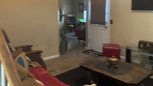 A living room with a sofa, a coffee table, and a television. There is a door leading to another room. - Enchanting Cottage Home nearby Airport (Conley)