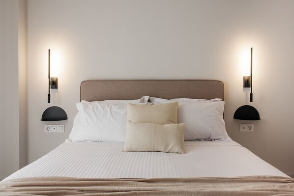 Un lit bien fait, recouvert d’une couvre-lit à rayures et d’un plaid beige, avec deux lampes de chevet fixées au mur de chaque côté.