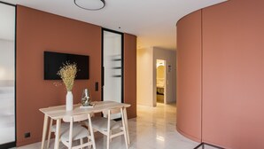 Un interior moderno con una mesa y sillas de madera, un televisor de pantalla plana montado en la pared y un pasillo que conduce a un baño.
