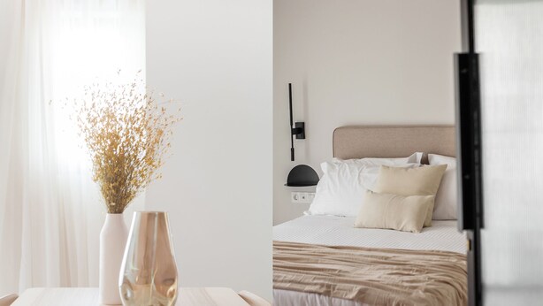 Un dormitorio con cama, mesita de noche y un jarrón con flores secas.