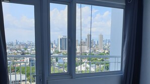 Ein Hotelzimmer mit einem großen Bett, Blick auf eine Stadtlandschaft durch eine Schiebetür und einem Tablett mit Handtüchern und einer Toilettenpapierrolle auf dem Boden.