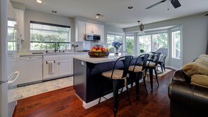A modern kitchen with white cabinets, a central island, and a dining area with black chairs. - Spacious Family Retreat near Botanica, Legoland, Frontwave Arena, & Beach! (Oceanside)