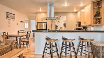 A modern kitchen with wooden cabinets, a stainless steel refrigerator, a central island with stools, and a decorative wall piece.