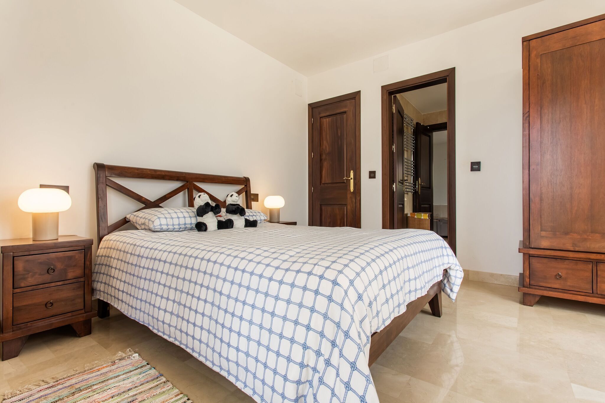 Une chambre à coucher comprenant un lit, des tables de chevet, une armoire en bois et une porte.