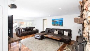 A modern living room with a fireplace, leather sofas, a coffee table, and a television. - Multi-Generation retreat! Pet friendly w/ fenced yard. 5 min to lake & trails. (Truckee)