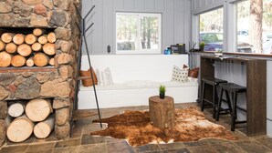 A cozy room with a stone fireplace, a large window, a wooden bench, and a cowhide rug. - Multi-Generation retreat! Pet friendly w/ fenced yard. 5 min to lake & trails. (Truckee)
