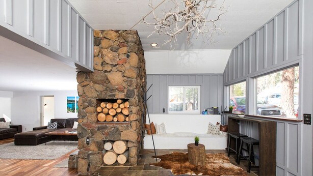 A modern living room with a stone fireplace, a large window, and a leather sofa. - Multi-Generation retreat! Pet friendly w/ fenced yard. 5 min to lake & trails. (Truckee)