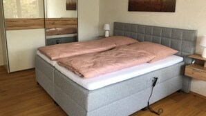 Ein modernes Schlafzimmer mit einem grau gepolsterten Bett, einem Nachttisch mit Lampe und einem großen Spiegel.