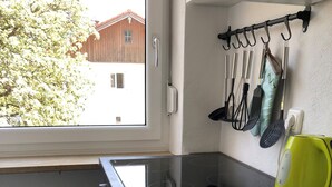 Eine Küche mit einer schwarzen Induktionskochplatte, einem gelben Wasserkocher und verschiedenen Küchenutensilien, die an einem Gestell hängen.
