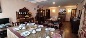 Un coin repas avec une table dressée pour quatre personnes, entourée de chaises en bois. Un téléviseur est fixé au mur, sur la gauche.