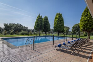 Une piscine dotée d’une terrasse carrelée, entourée d’une clôture et équipée de chaises longues.