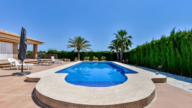 A rectangular swimming pool with a curved edge, surrounded by a stone deck. There are lounge chairs and a covered area with an umbrella. - Villa for rent in Calpe AZORIN for 6 pax, with private pool. (Calpe)