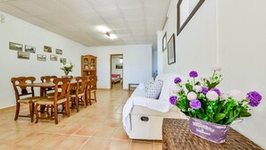 A dining area with wooden chairs and a table, a white sofa, and a vase of flowers on a table. - Villa for rent in Calpe AZORIN for 6 pax, with private pool. (Calpe)