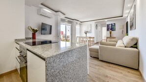 Una cucina moderna con piani in granito, forno integrato e zona pranzo con tavolo e sedie bianche.