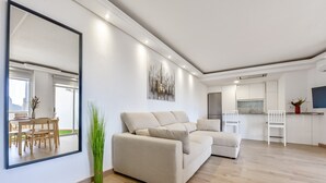 Un soggiorno moderno con un'ampia sezione angolare, un'area pranzo con tavolo e sedie e una cucina con pensili bianchi e un frigorifero.