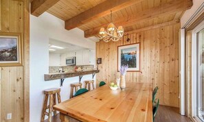 Un coin repas en bois avec une longue table, des chaises et un lustre.
