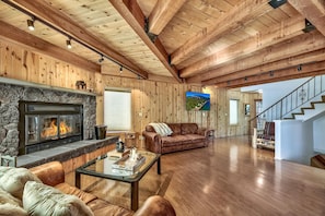 A spacious living room with a stone fireplace, leather sofas, wooden floors, and a staircase.