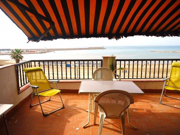 A terrace with a table and chairs, overlooking a beach and sea.
