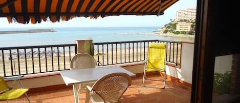 A balcony with a view of the sea, a table, and two chairs.