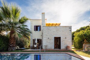 A two-story house with a swimming pool, stone walls, and a patio with outdoor furniture.