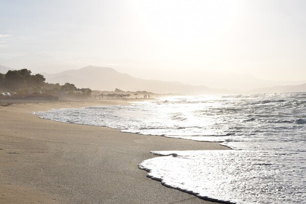 A beach with waves, a clear sky, and distant mountains.
