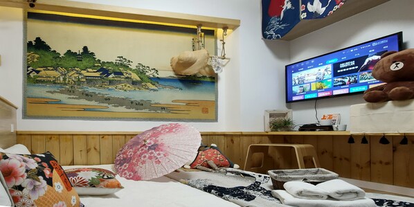 Una habitación con una pintura tradicional japonesa, un televisor mostrando varios canales y un osito de peluche grande.