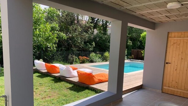 Un espace extérieur abrité comprenant une piscine, une terrasse en bois et un coin salon avec des coussins.