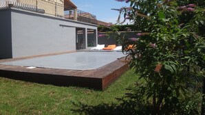 Un espace extérieur moderne, aménagé en terrasse avec un revêtement de sol en bois, un mur gris et une rambarde en métal.