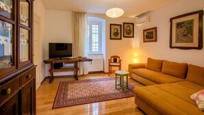 A living room with a sofa, a television, a small table, and a chair. There are framed pictures on the wall and a window with curtains. - Attractive holiday home in Kraljevica with garden (Kraljevica)