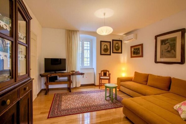 A living room with a sofa, a television, a small table, and a chair. There are framed pictures on the wall and a window with curtains. - Attractive holiday home in Kraljevica with garden (Kraljevica)