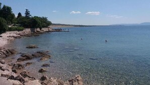 A rocky shoreline with clear water, a pier, and distant mountains. - Attractive holiday home in Kraljevica with garden (Kraljevica)
