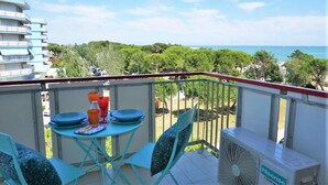A balcony with a table set for dining, a fan, and a view of the sea and greenery.