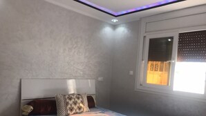 Ein Schlafzimmer mit einem Bett, Kissen mit Muster, einem Fenster mit Jalousien und einer Deckenleuchte.