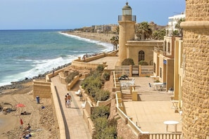 A coastal hotel with a beach view, a lighthouse, and a patio area with outdoor seating.
