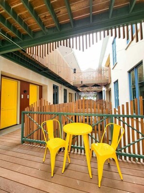 Un espace extérieur abrité, doté d’un plancher en bois, de chaises jaunes et d’une rambarde verte.