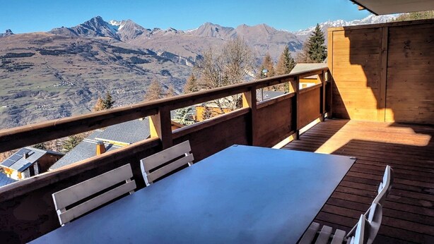 Eine Holzterrasse mit Tisch und Stühlen mit Blick auf eine gebirgige Landschaft.