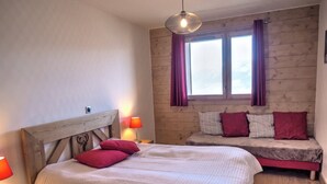 Ein Schlafzimmer mit einem Bett mit Holz-Kopfschild, einem Nachttisch mit Lampe, einem Fenster mit Vorhängen und einer Bank mit Kissen.