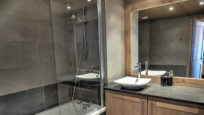 Ein modernes Badezimmer mit einer Duschkabine aus Glas, einem weißen Waschbecken und Holzschränken.
