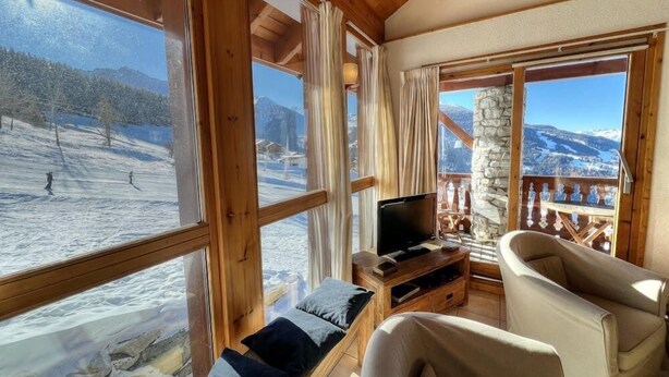 A cozy room with large windows offering a view of a snowy mountain landscape.