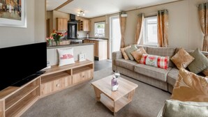 A modern living room with a flat-screen TV, wooden furniture, a sofa with cushions, and a coffee table. - Golf View by Interhome (Nairn)