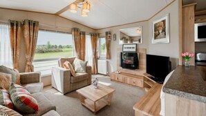 A modern RV interior with a living area, kitchenette, and a large window offering a view of the outdoors. - Golf View by Interhome (Nairn)