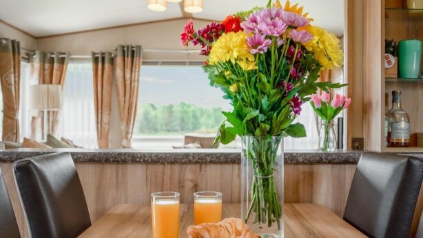A breakfast setting with croissants, juice, and a floral centerpiece on a wooden table. - Golf View by Interhome (Nairn)