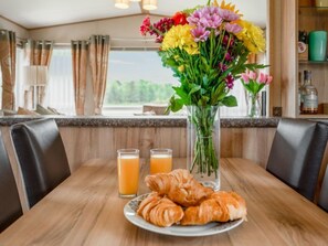 A breakfast setting with croissants, juice, and a floral centerpiece on a wooden table. - Golf View by Interhome (Nairn)