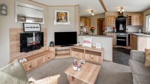 A compact living space with a TV, wooden furniture, a kitchen area, and a dining table. - Golf View by Interhome (Nairn)