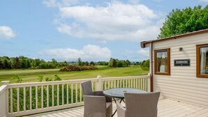 A covered outdoor area with a table and chairs, a sign reading "Amhieside," and a view of a golf course. - Golf View by Interhome (Nairn)